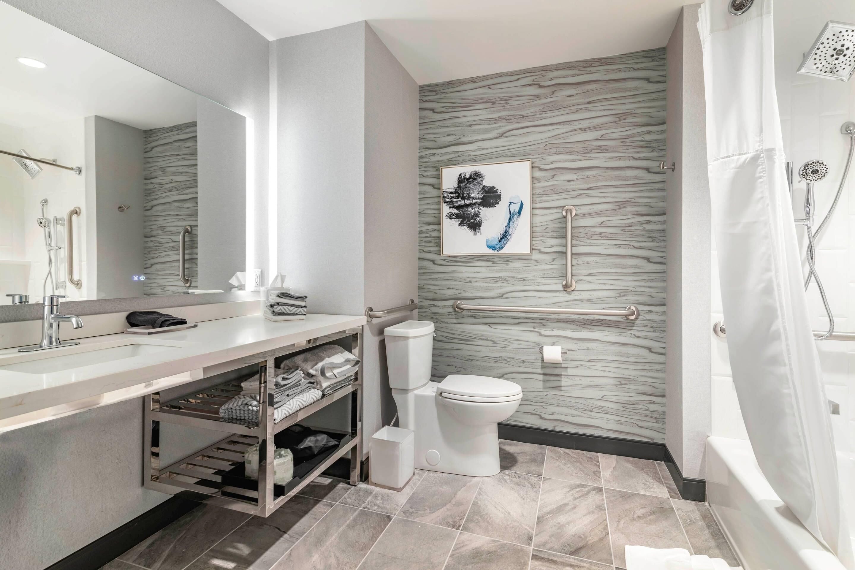 A modern bathroom with a marble backsplash, a toilet, a sink with a vanity, and a shower area.