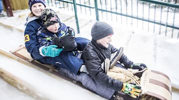 Three children sledding on a wooden track with snow on the ground.