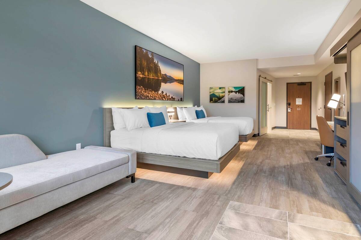 A modern hotel room with a large bed, a sofa, and a desk.