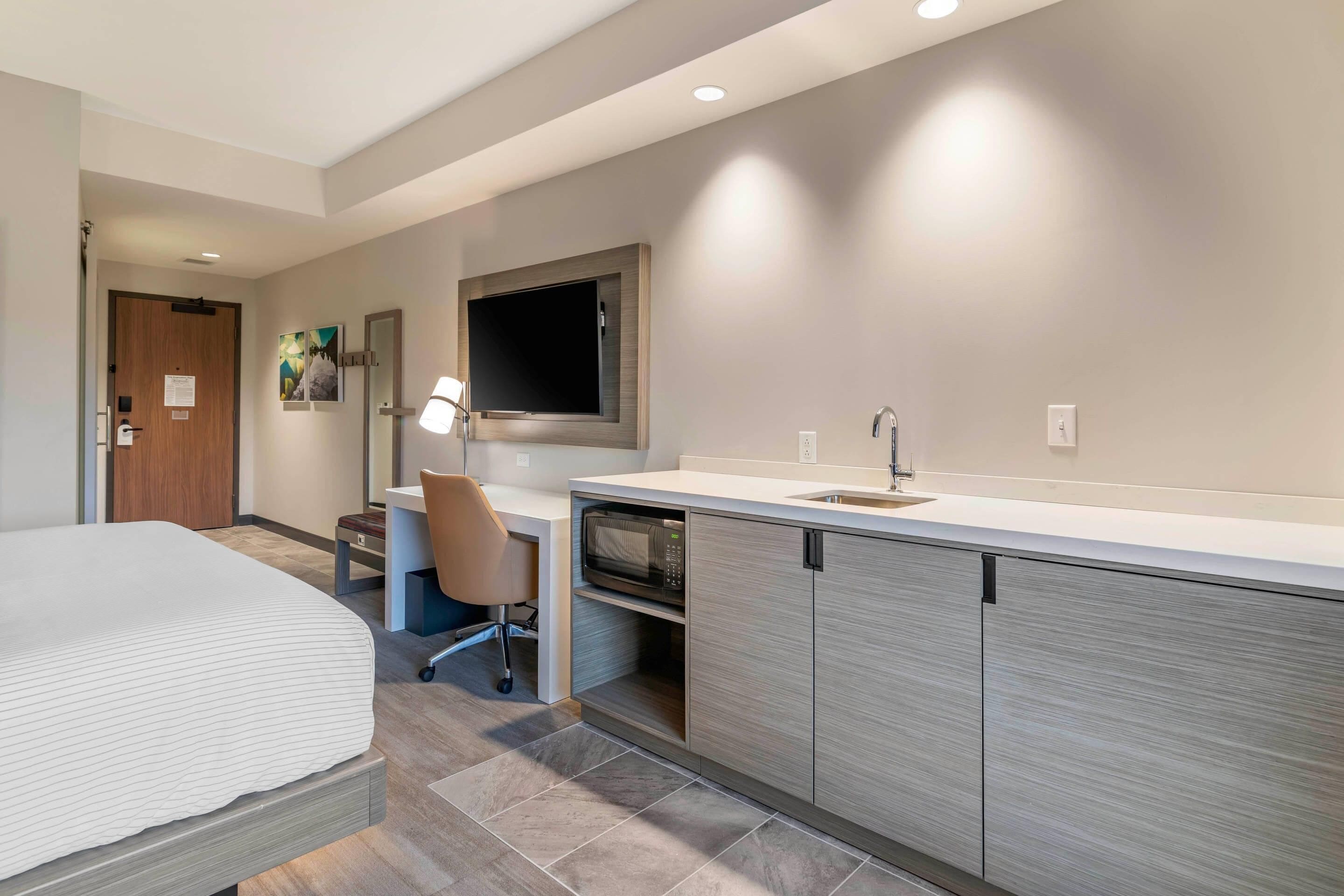 Une chambre d’hôtel moderne équipée d’un lit, d’un bureau, d’un four à micro-ondes et d’un lavabo intégré.