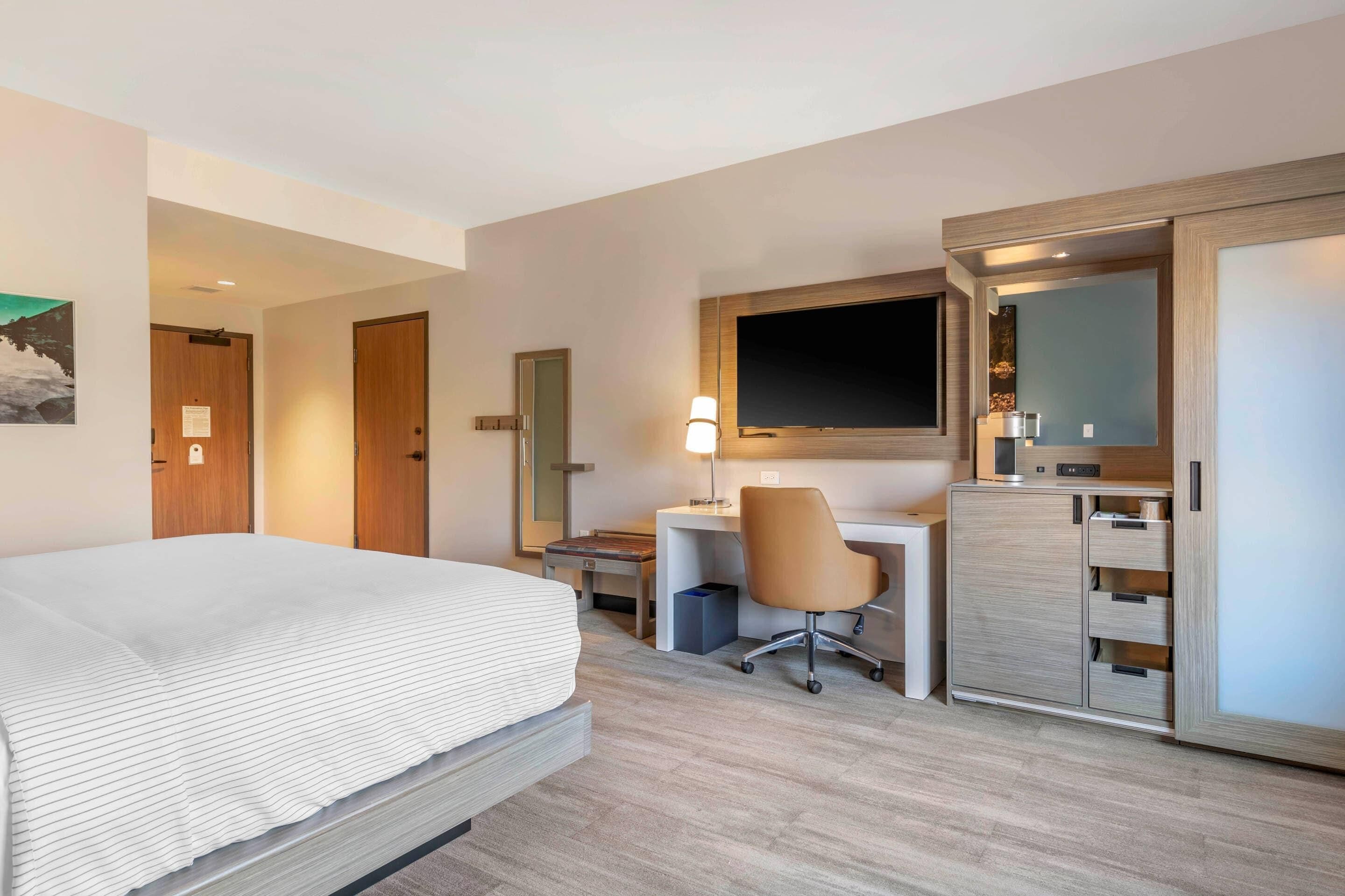 A hotel room with a bed, desk, chair, and wardrobe.