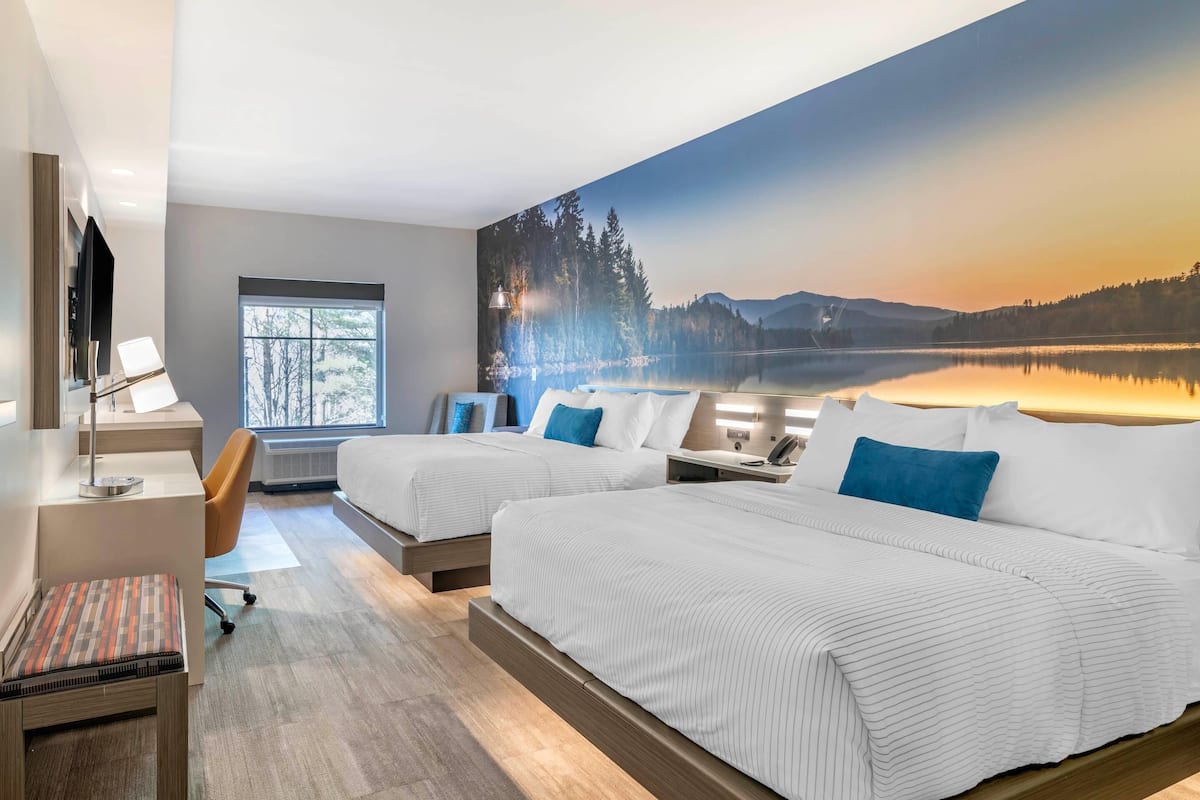 A hotel room with two beds, a desk, a chair, a TV, and a large window.