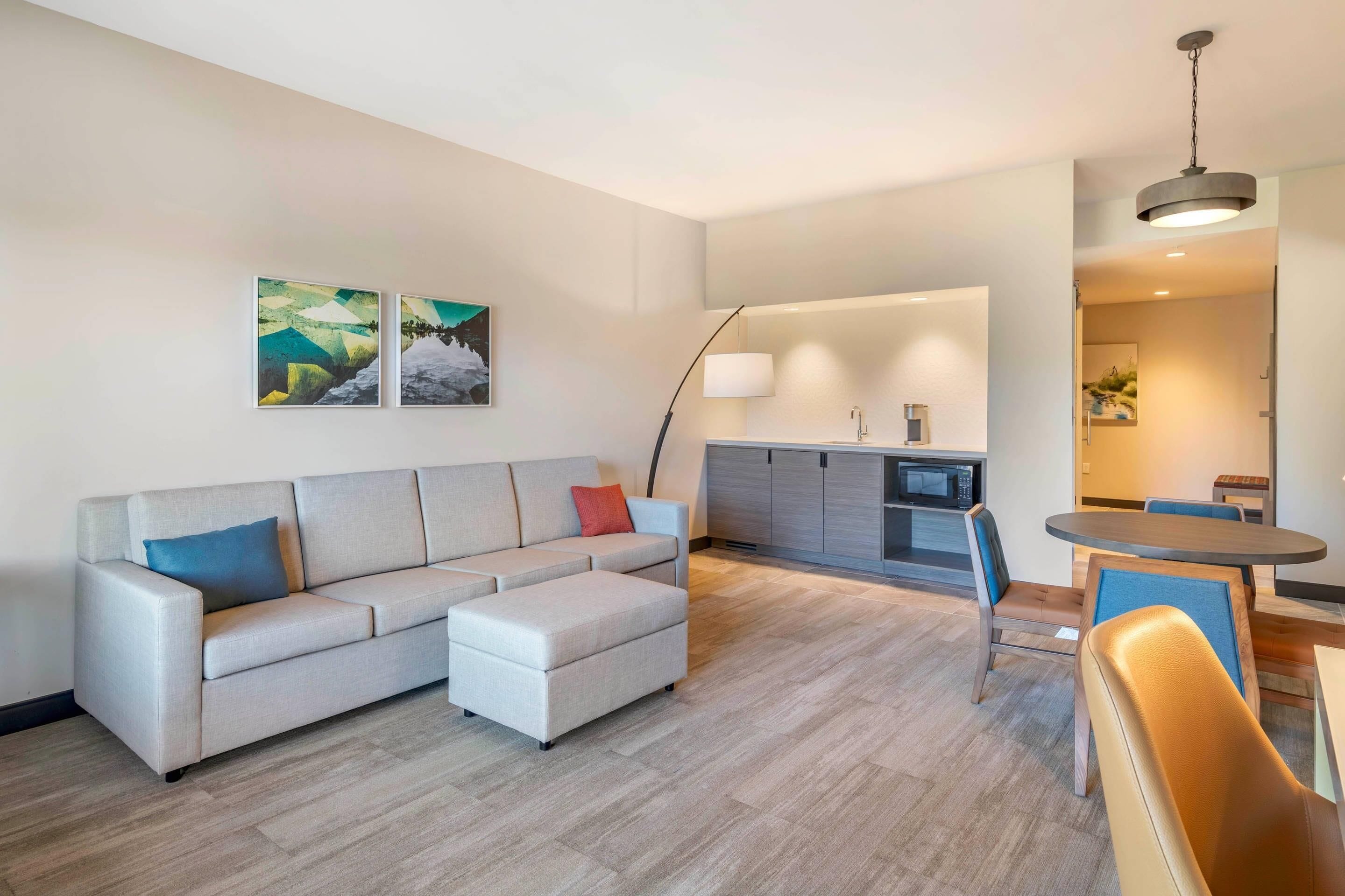A modern living room with a sectional sofa, a dining table with chairs, and a kitchen area in the background.