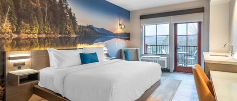A modern hotel room with a large bed, a desk, and a view of a lake through the window.