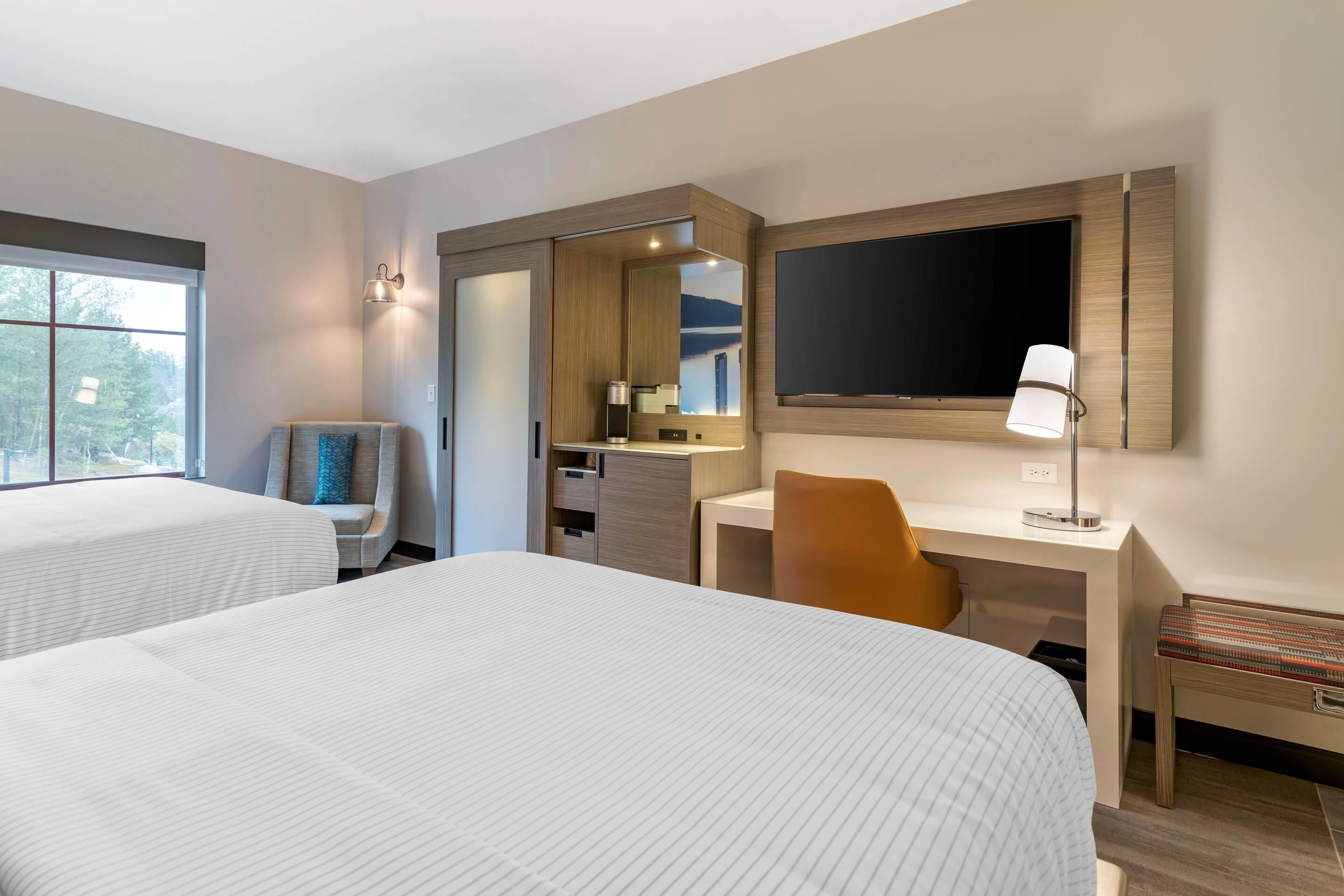 Ein Hotelzimmer mit zwei Betten, einem Schreibtisch, einem Stuhl, einem Fernseher und einem Fenster.