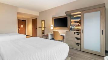 A hotel room with a large bed, a desk with a chair, a TV mounted above the desk, and a wardrobe.