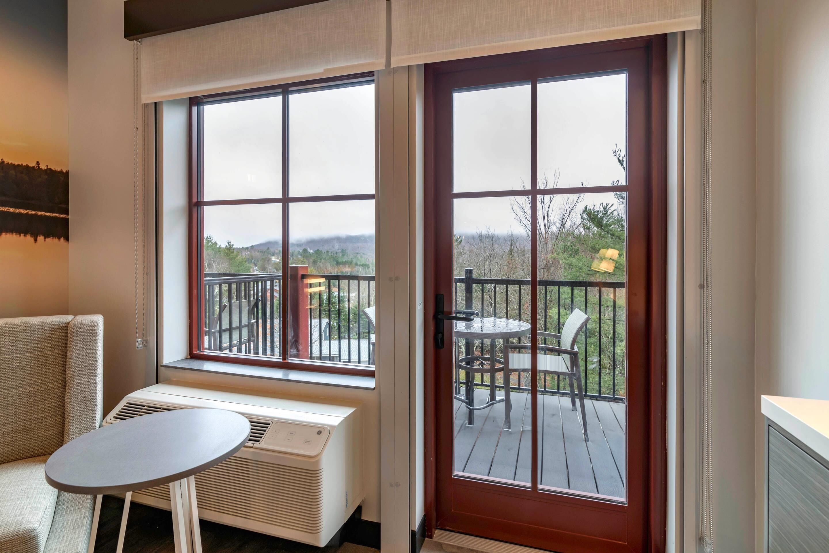 A room with a sofa, a small table, and a large window with a view of a deck and outdoor scenery.
