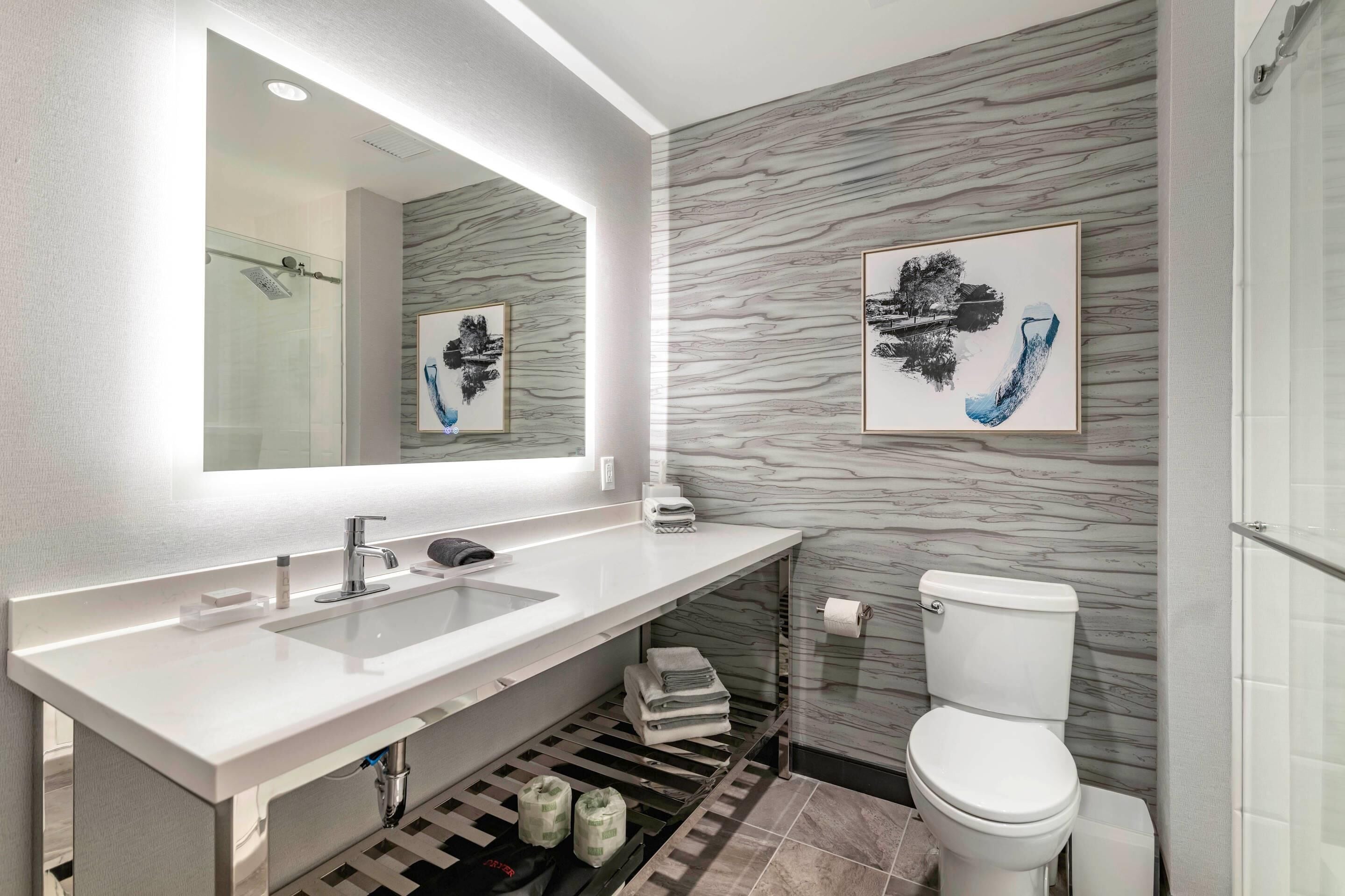 Un baño moderno con un lavabo blanco, un espejo y un inodoro. Hay dos obras de arte enmarcadas en la pared.