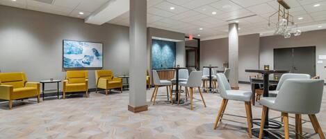 A modern hotel lobby with a herringbone-patterned floor, yellow and gray seating, and a contemporary chandelier.