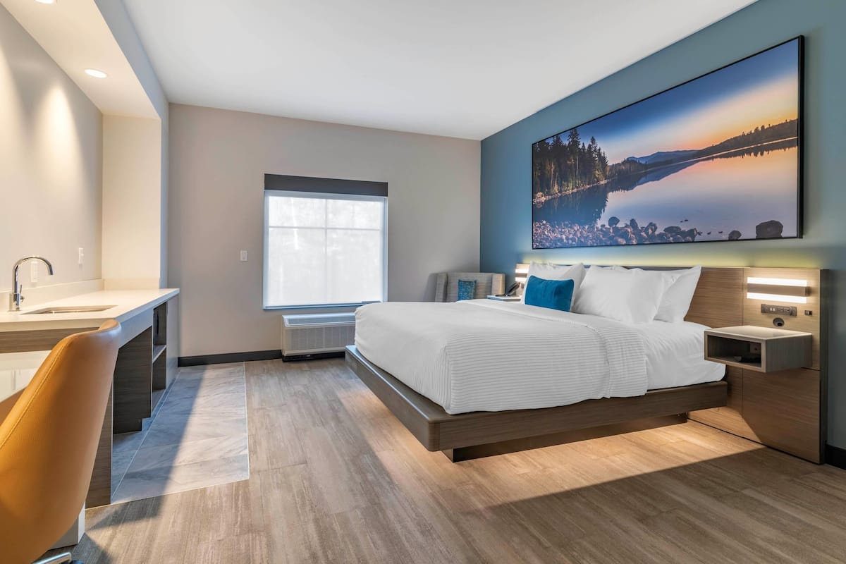A modern hotel room with a large bed, a desk, and a window with blinds.