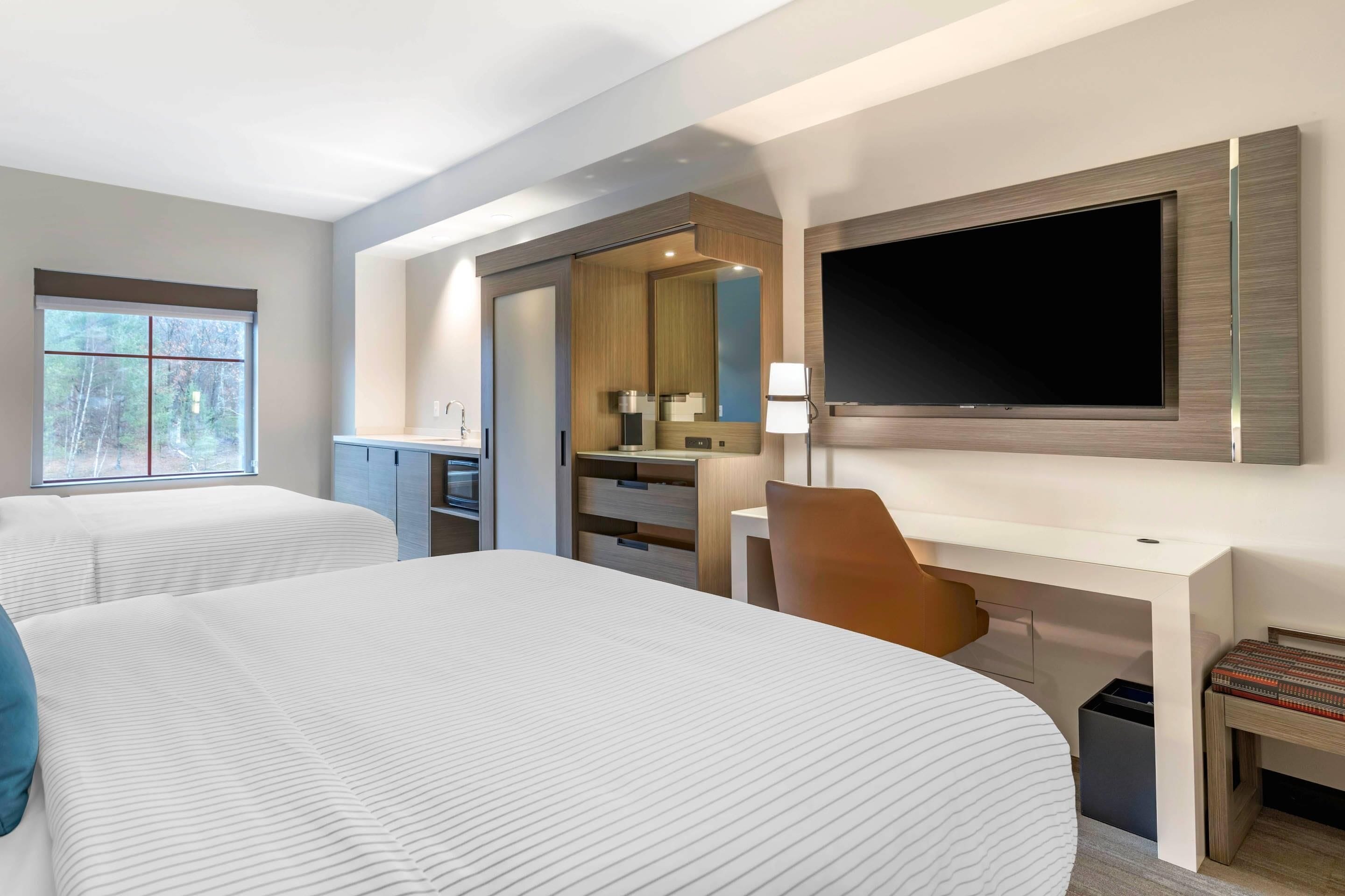 A hotel room with two beds, a desk, a TV, and a bathroom.