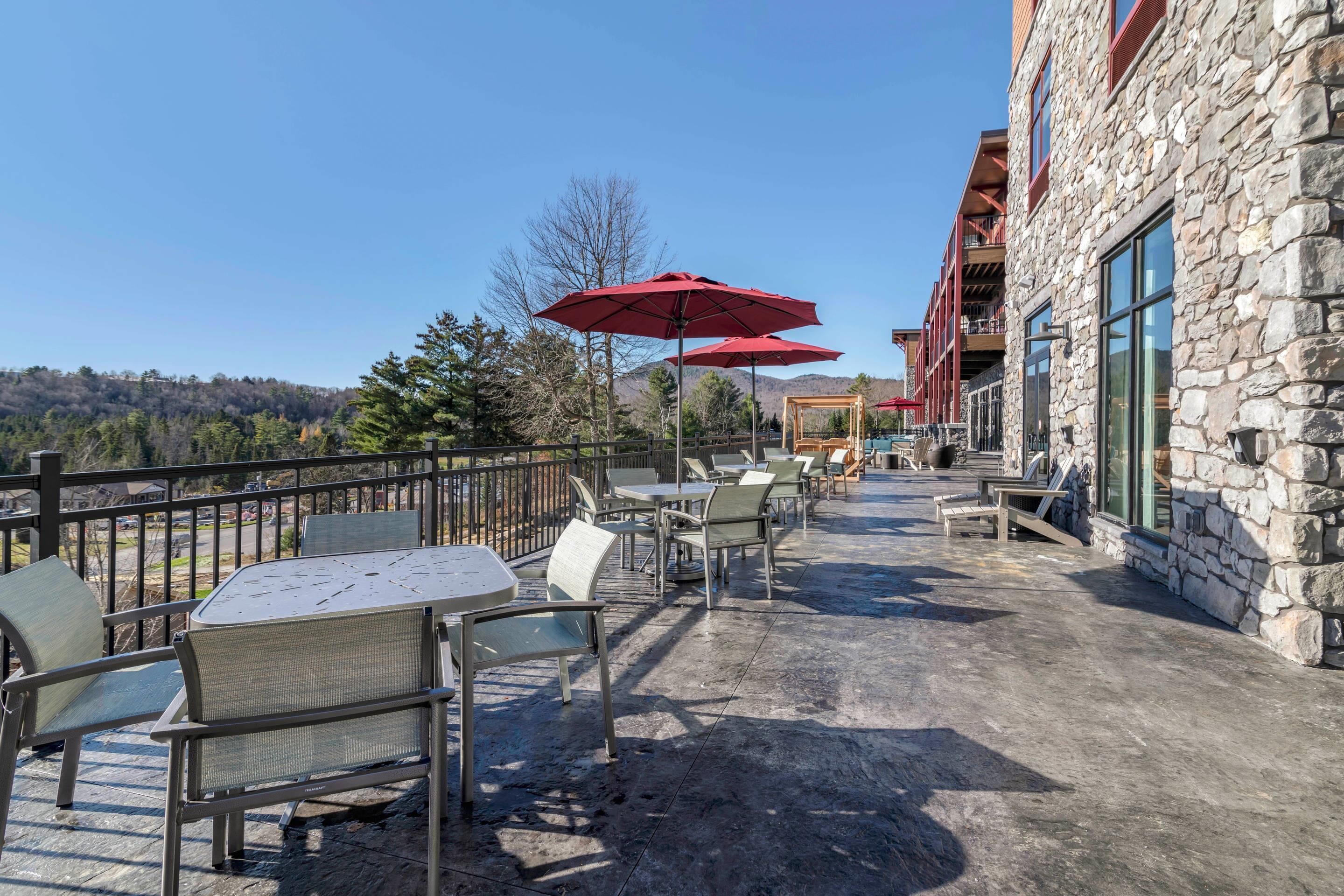 Une terrasse extérieure avec des tables et des chaises, des parasols rouges et un bâtiment en pierre doté de grandes fenêtres.