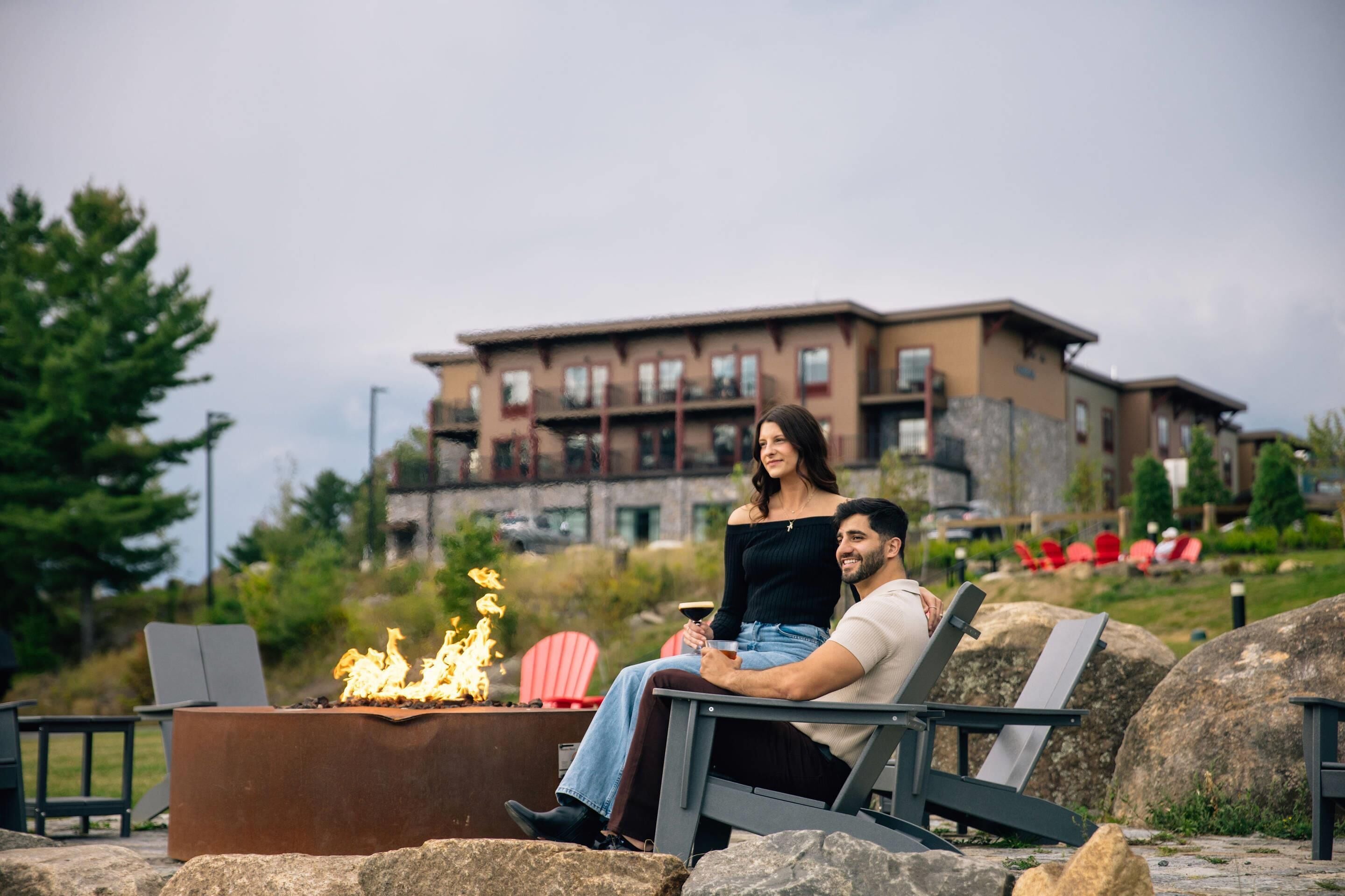 A couple sitting by a fire pit with a view of a multi-story building in the background.
