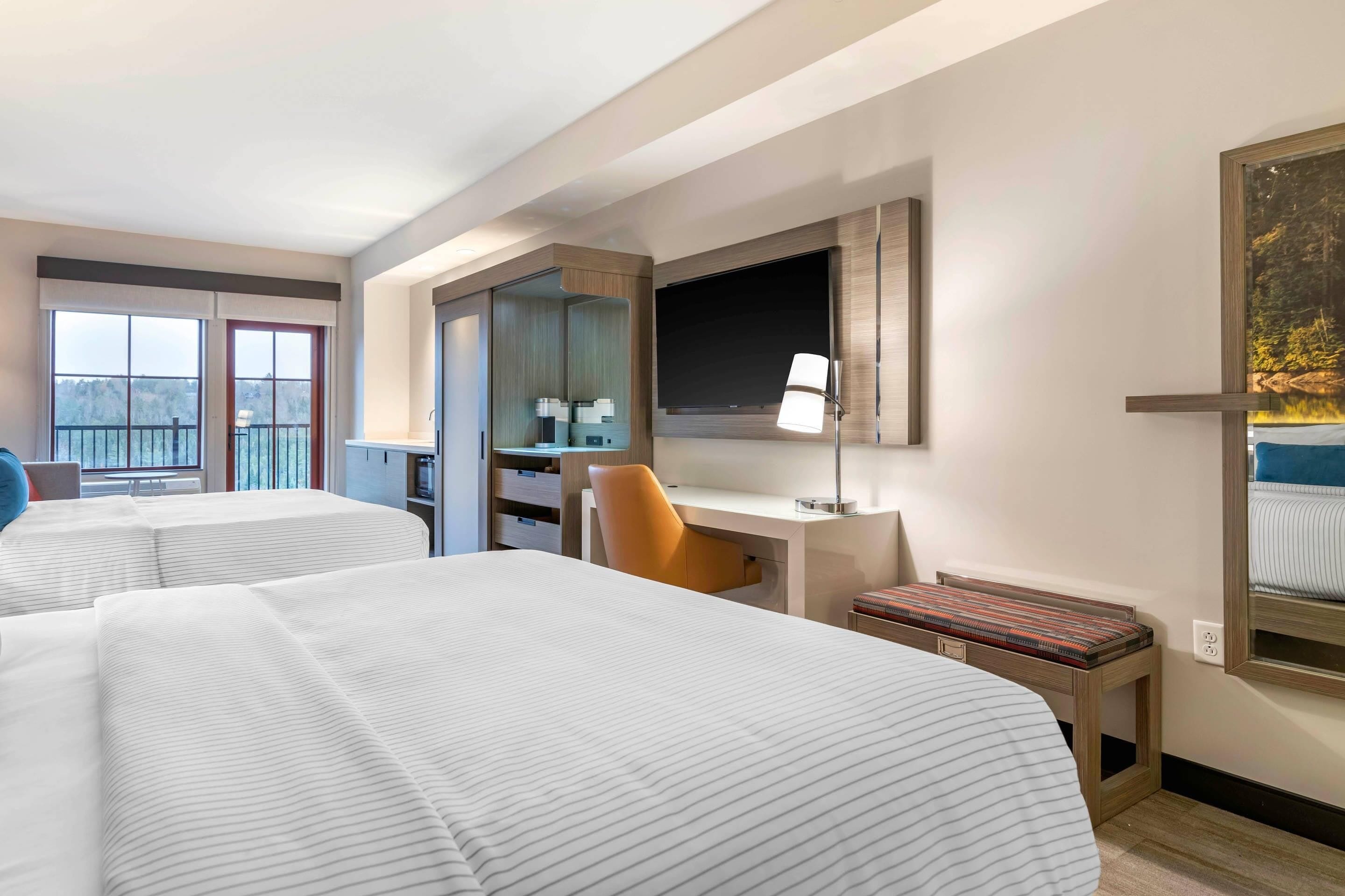 Une chambre d’hôtel avec deux lits, un bureau, une chaise, une télévision et une fenêtre donnant sur un beau paysage.