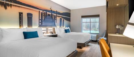 Habitación de hotel con dos camas, un gran mural de un atardecer sobre un muelle, una ventana con vistas a árboles y un escritorio moderno con una lámpara.
