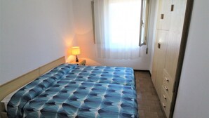 Una camera con un letto, un comodino con lampada, un armadio e una finestra con tende.