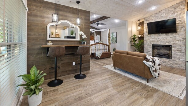 Una sala de estar moderna con techo de madera, chimenea de piedra, televisor montado en la pared y una zona de bar con taburetes.
