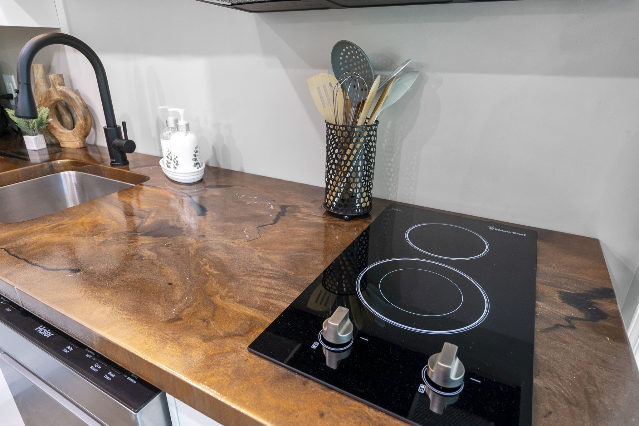 Une cuisine équipée d’un évier en acier inoxydable, d’une plaque de cuisson à induction noire et d’une planche à découper en bois.