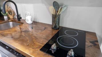 Une cuisine équipée d’un évier en acier inoxydable, d’une plaque de cuisson à induction noire et d’une planche à découper en bois.