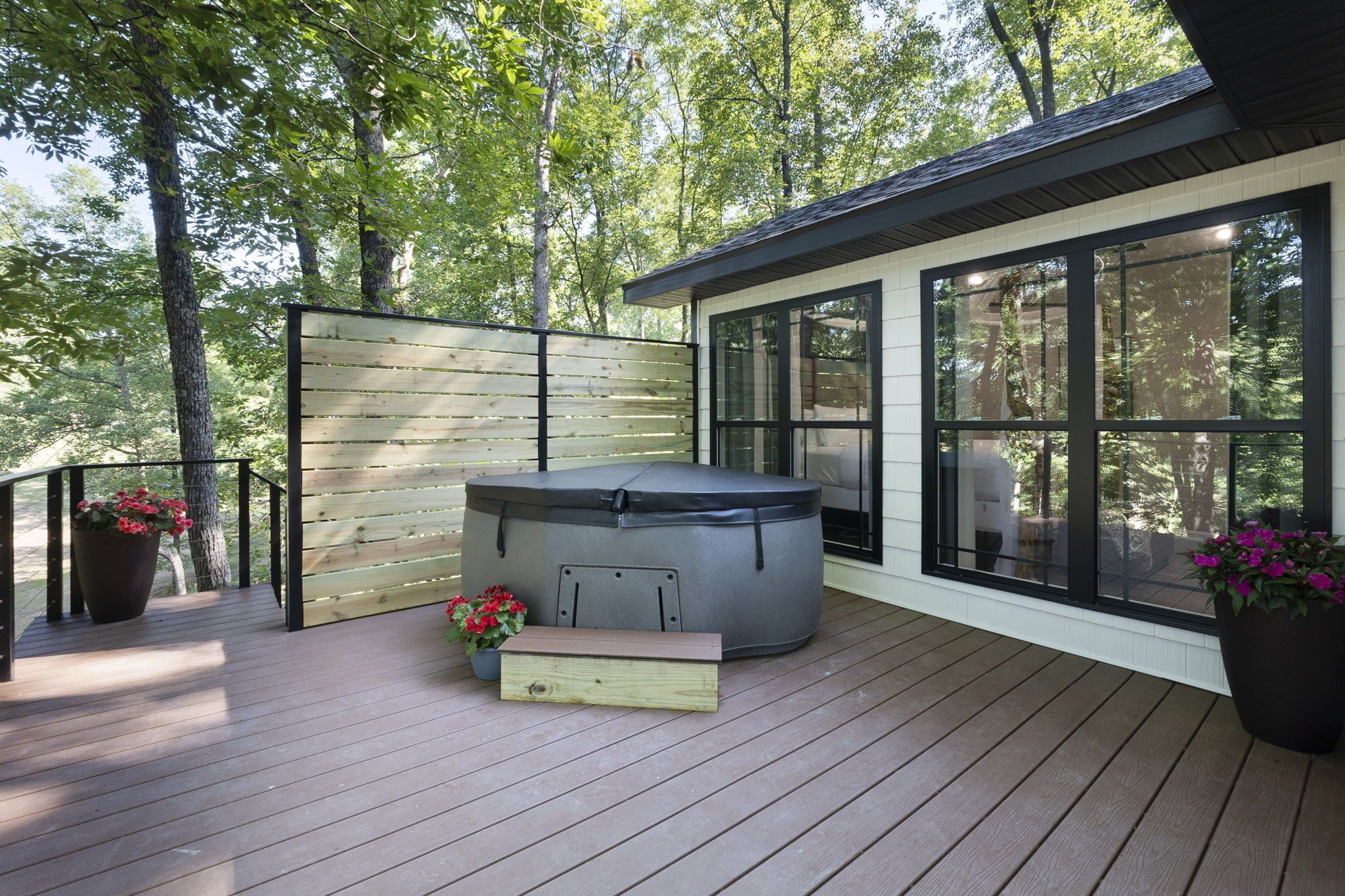 Een terras met een hottub, houten omheining en potplanten.