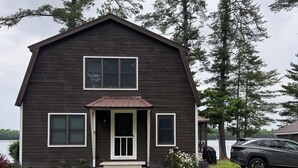 Une maison en bois à deux étages, dotée d’un porche à l’avant, d’un garage et d’une voiture garée à proximité.