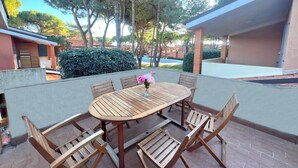 Patio esterno con tavolo rotondo in legno e sei sedie, circondato da un muretto in mattoni.