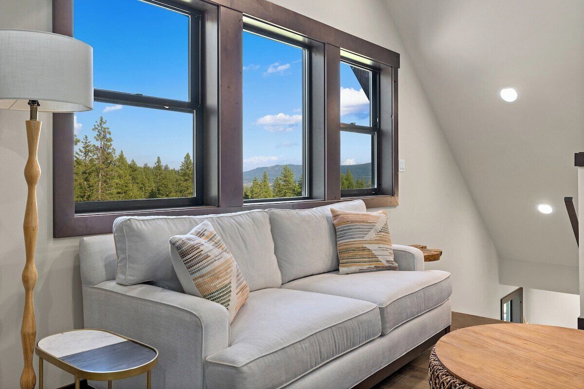 A modern loft bedroom with a large window, a sofa, a small table, and a lamp.