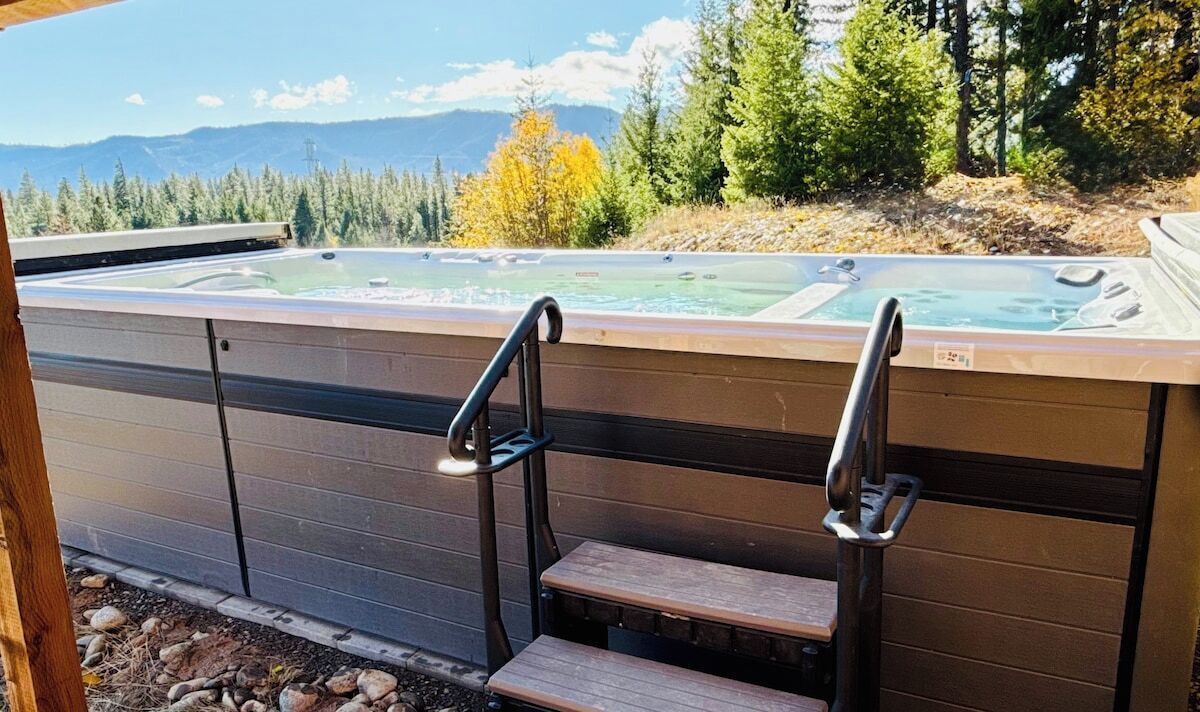 Un bain à remous avec des marches menant à celui-ci, entouré d’une terrasse en bois et offrant une vue sur les arbres et les montagnes.
