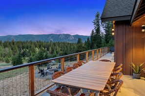 A wooden deck with a table and chairs, overlooking a forested mountain range.