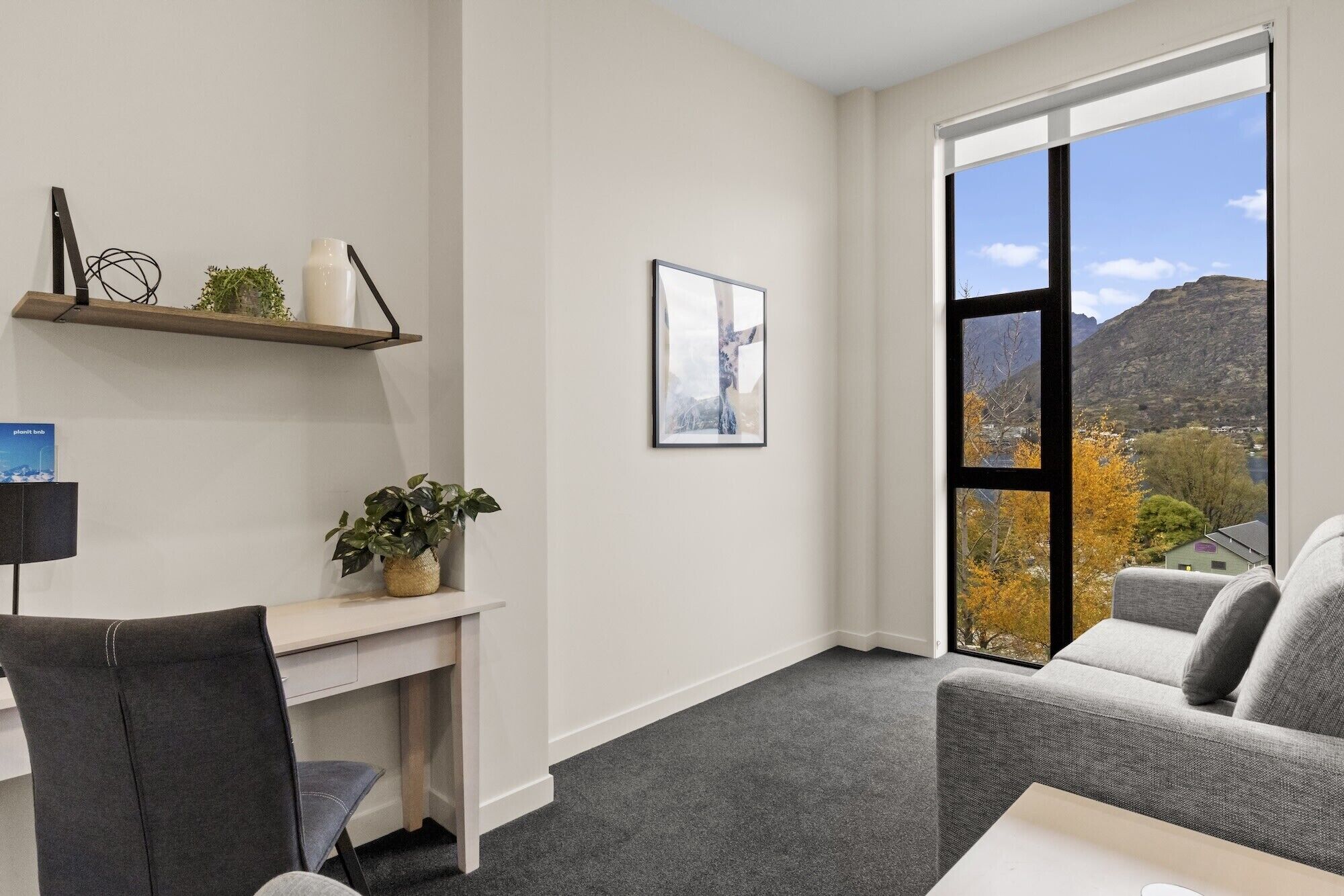 A modern office space with a desk, chair, and a large window offering a view of a mountainous landscape.