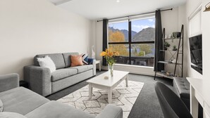 Un salon moderne avec un canapé gris, une table basse blanche et une vue sur les montagnes, visible à travers de grandes fenêtres.