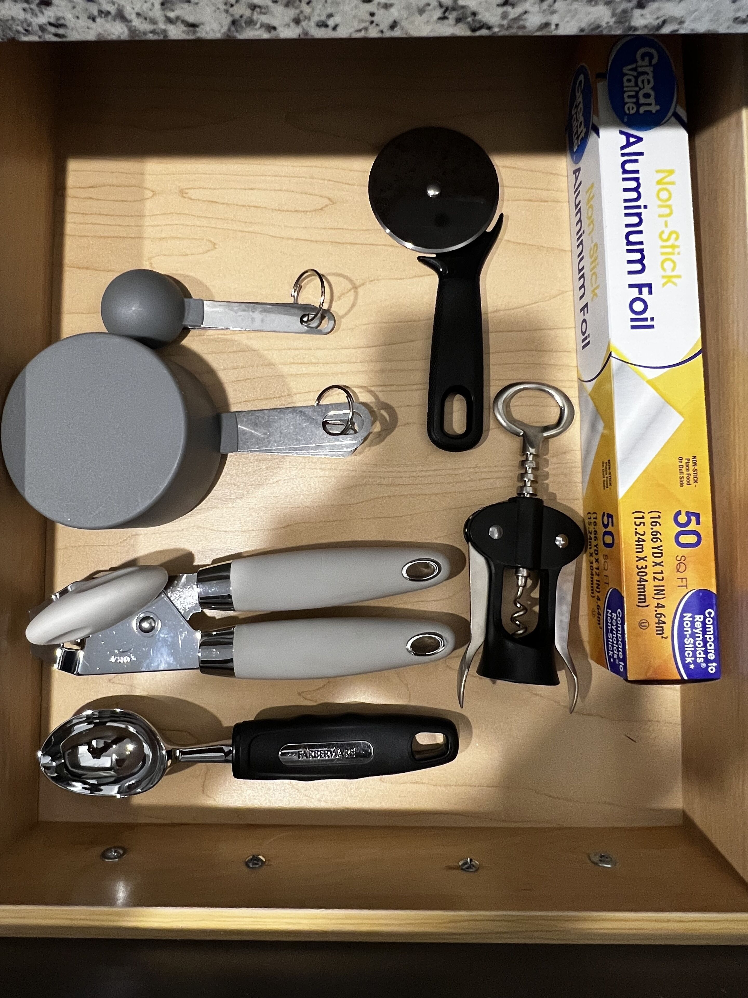 A drawer containing various kitchen utensils and a box of non-stick aluminum foil.