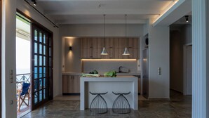 A modern kitchen with a central island, pendant lights, and a view to a balcony. - Luxury Seaview Apartment, 1min Walk From Beach! (Apokoronas)