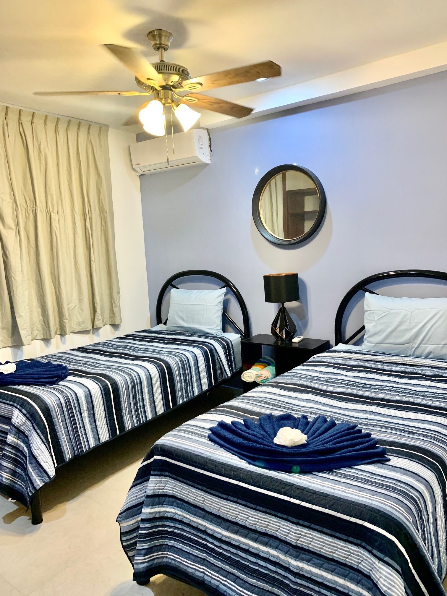 Ein Hotelzimmer mit zwei Betten, einem Deckenventilator, einem Spiegel und einer Klimaanlage.