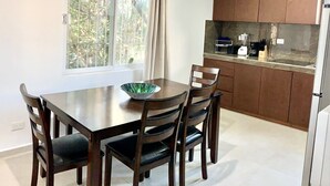 Un comedor con mesa y sillas, una ventana con cortinas, y una cocina con armarios y electrodomésticos.