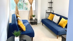 Un salón con dos sofás azules, un ventilador de techo, una mesita con una planta y una ventana con cortinas.