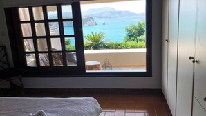 A bedroom with a large window overlooking a coastal view, a bed with a white cover, and a tiled floor. - Coco Seaview Apartment, 60sec Walk From Beach! (Apokoronas)