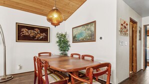 A dining area with a wooden table and chairs, surrounded by framed artwork, a floor lamp, and a potted plant.