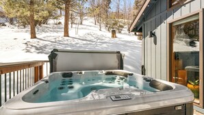 A hot tub on a wooden deck with a snowy landscape and trees in the background.