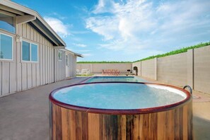 Un jardin avec un jacuzzi en bois, une piscine et une maison dotée d’un toit en pente.