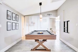 Une table de billard avec un cadre en bois, un luminaire suspendu et des tableaux encadrés accrochés au mur.