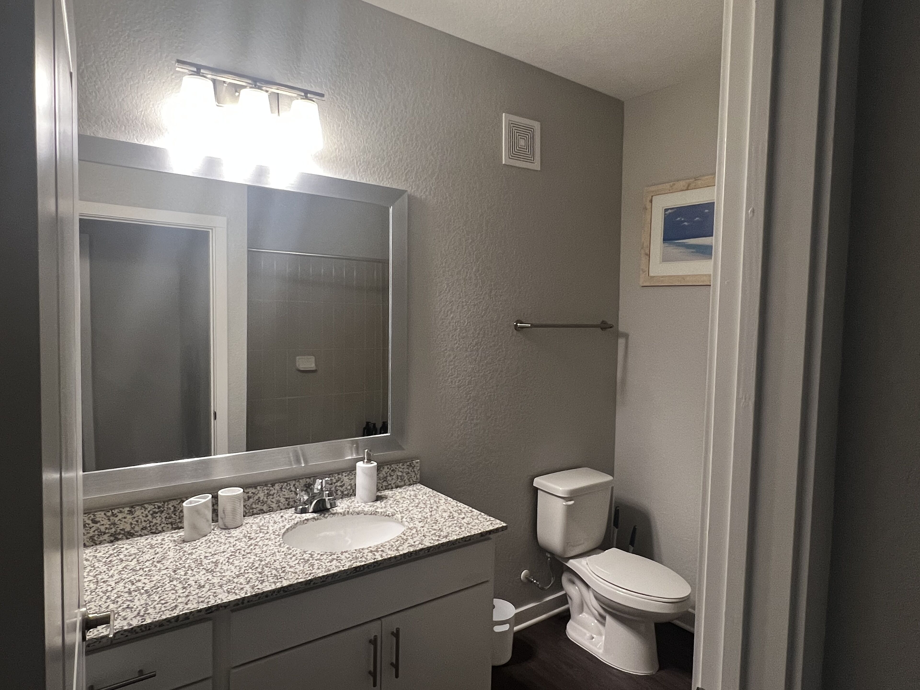 A bathroom with a sink, mirror, toilet, and shower.