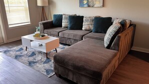 A living room with a sectional sofa, a side table, a lamp, and a painting on the wall.