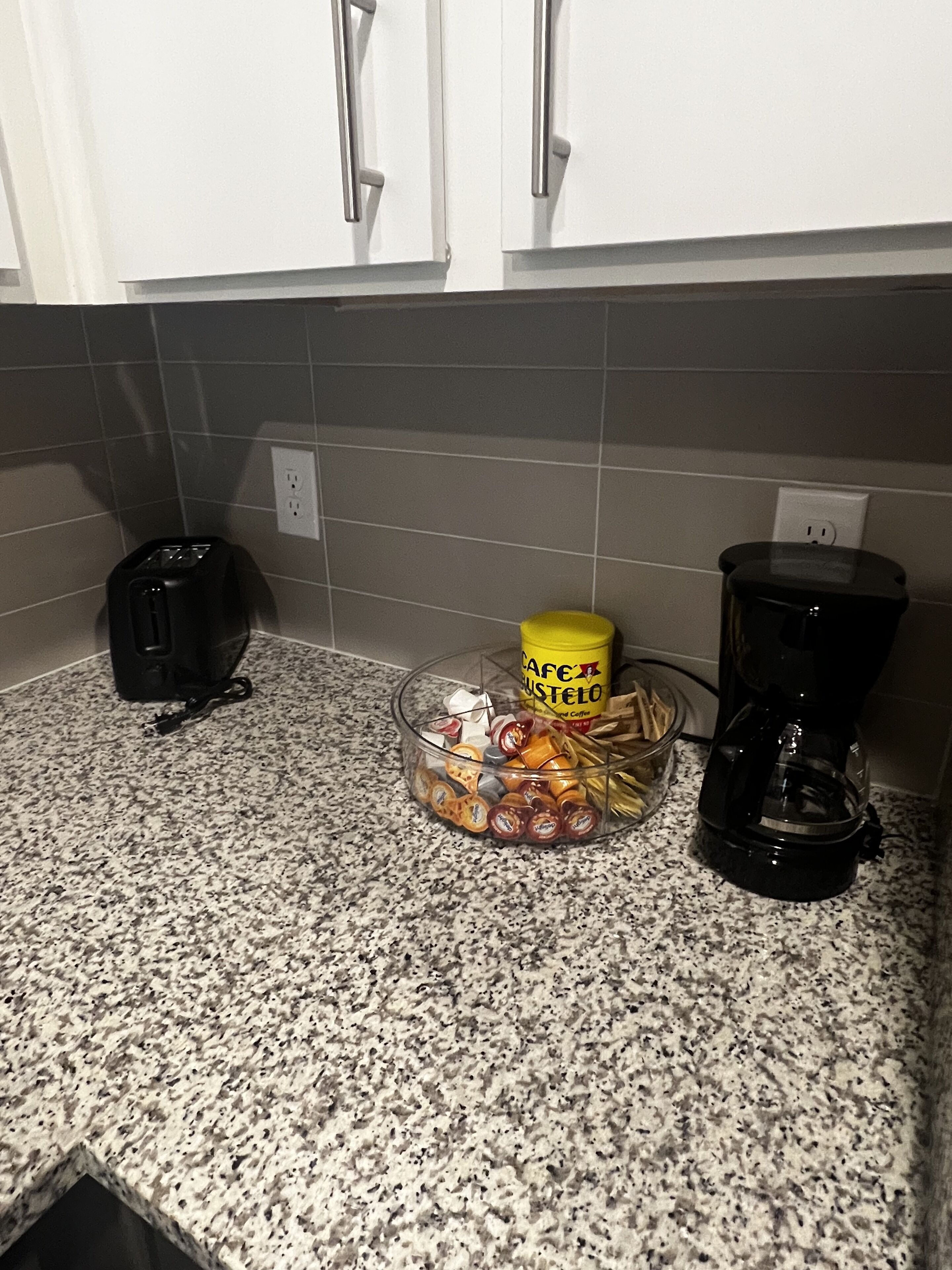 A kitchen counter with a toaster, a coffee maker, and a container of coffee pods.