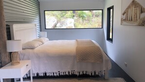 Une chambre à coucher avec un lit, une table de chevet, une lampe, une grande fenêtre et un tableau encadré au mur.