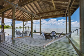 Eine Holzterrasse mit einer Hängematte, Korbstühlen und einem Tisch mit Blick auf ein Gewässer.
