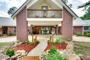 A two-story brick building with a balcony, a covered patio, and a stone pathway leading to the entrance. - Broken Bow Vacation Rental w/ Pool & Hot Tub! (Broken Bow)