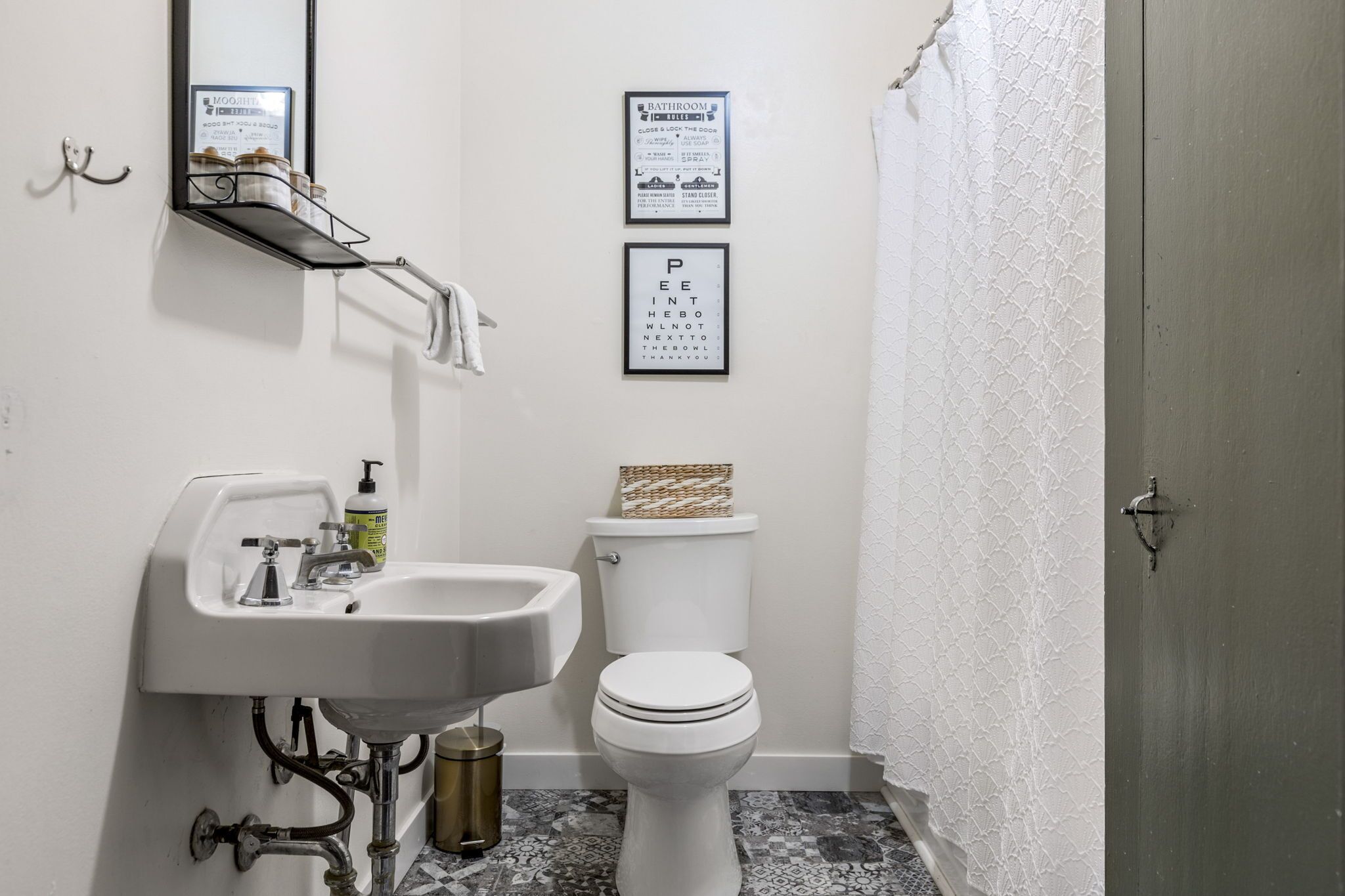 A bathroom with a white sink, toilet, and a mirror above the sink. There are two framed signs on the wall, one with a bathroom symbol and one with an eye chart.