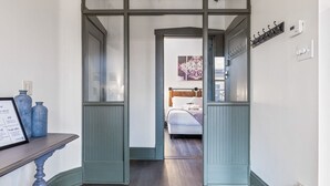 Een gang die leidt naar een slaapkamer met een bed, een kapstok en een wandthermostaat.