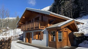 A wooden chalet with a balcony, large windows, and a snow-covered driveway. - Chalet Le Castor: in the center of Chatel (Châtel)